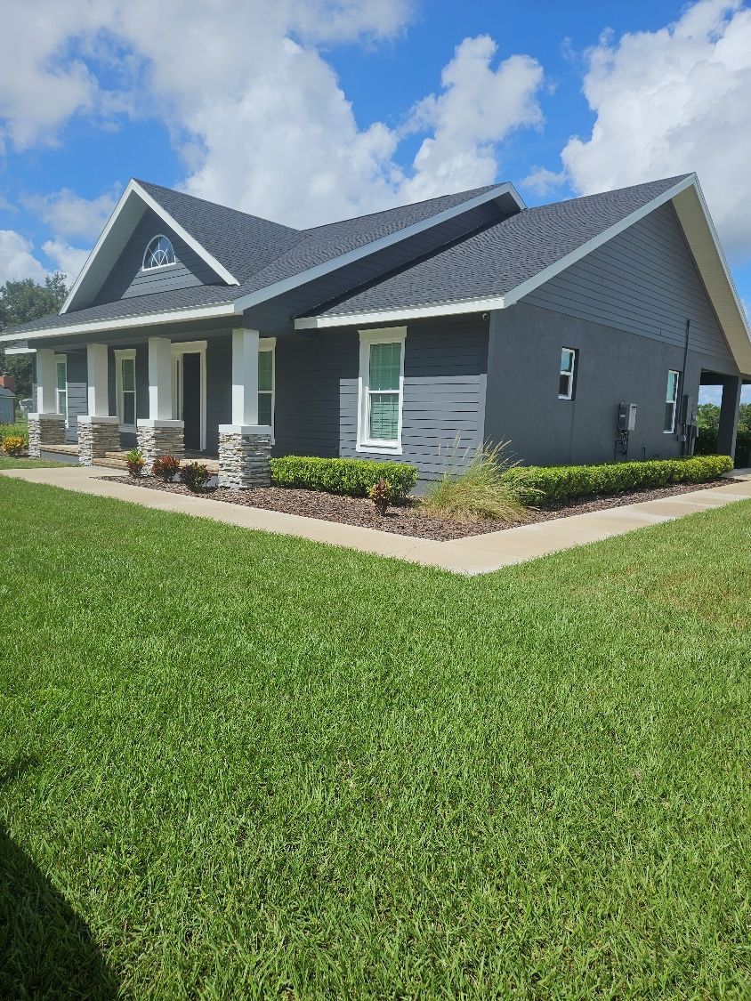 Gray single-story house with a dark roof, white trim, and a green lawn under a blue sky.