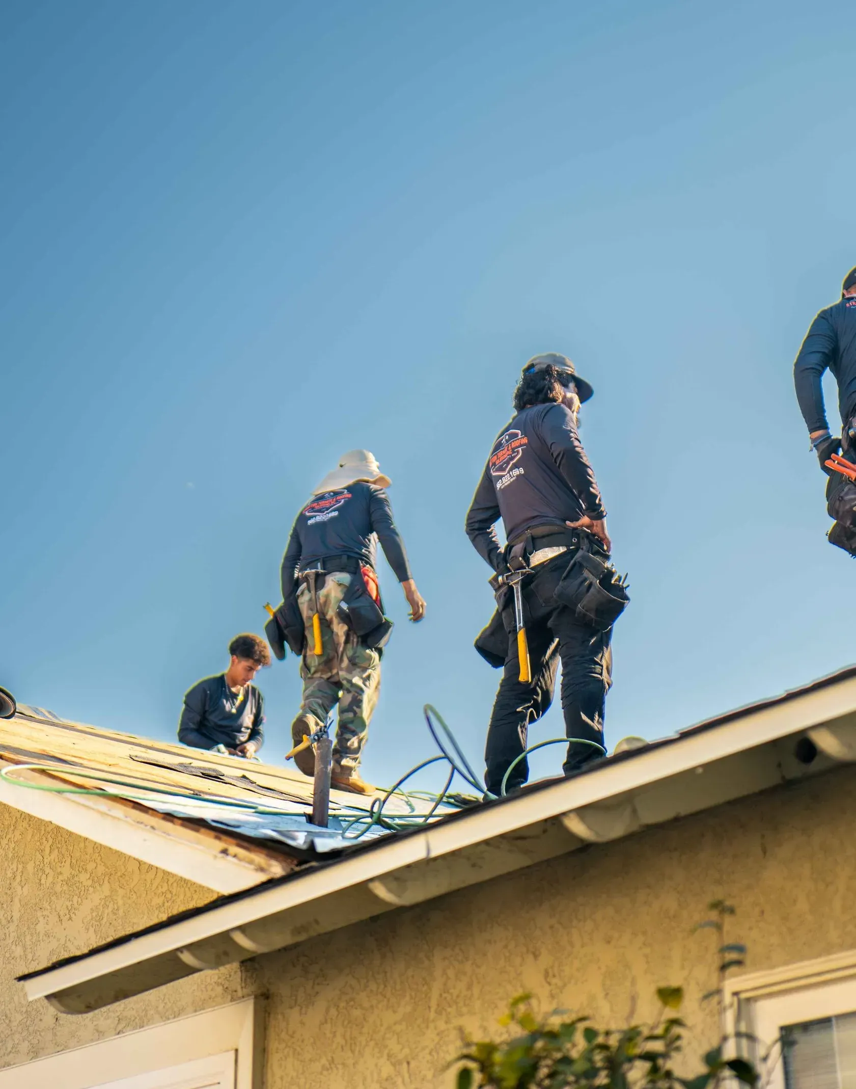 Roofers working on a residential roof under a clear, blue sky.