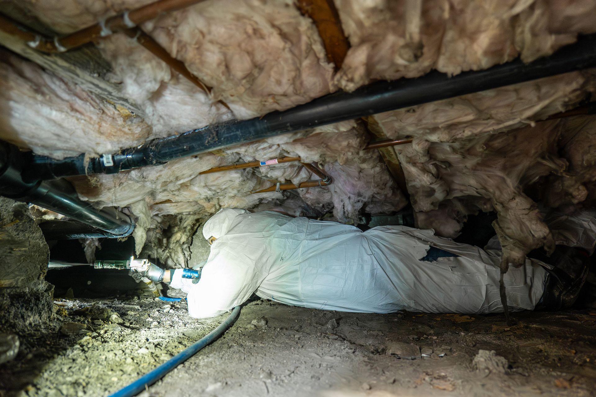 A person in a protective suit is crawling under a house.