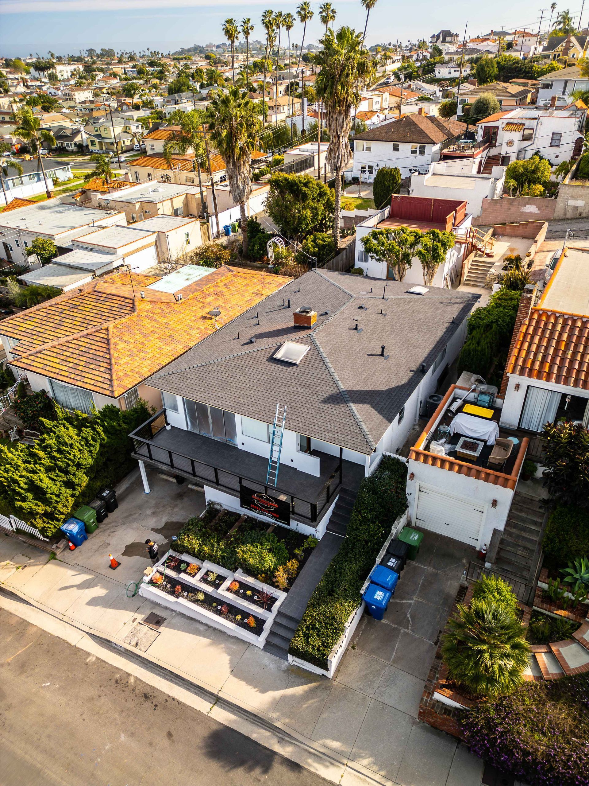 Aerial view of houses with gardens, rooftops, and palm trees. Sunny day.