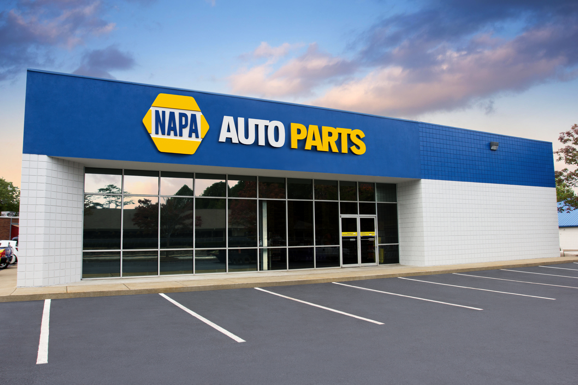 NAPA Auto Parts store exterior, blue and white facade, glass windows, empty parking spots.