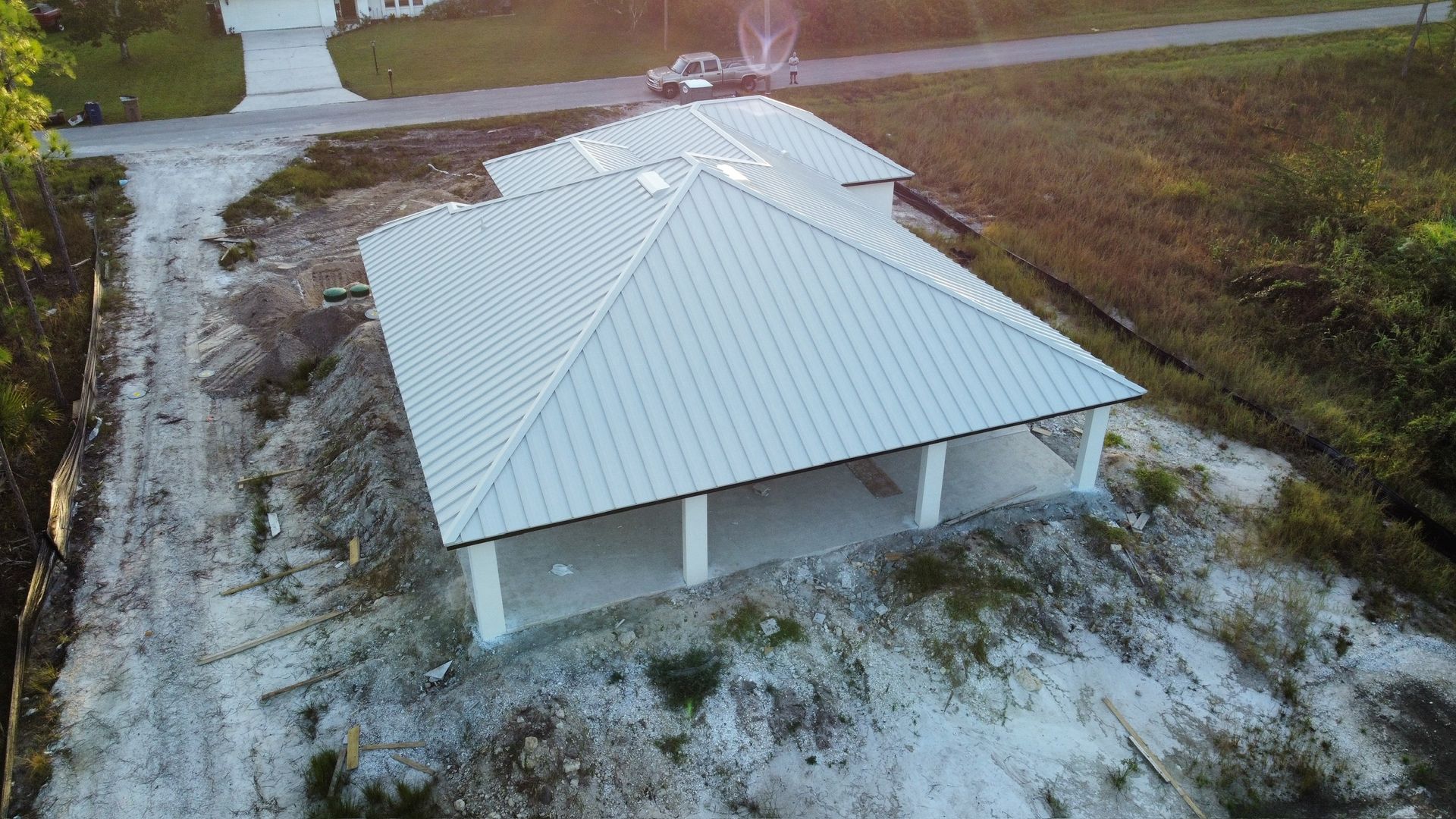 Aerial view of a new, light-colored building with a metal roof under construction.