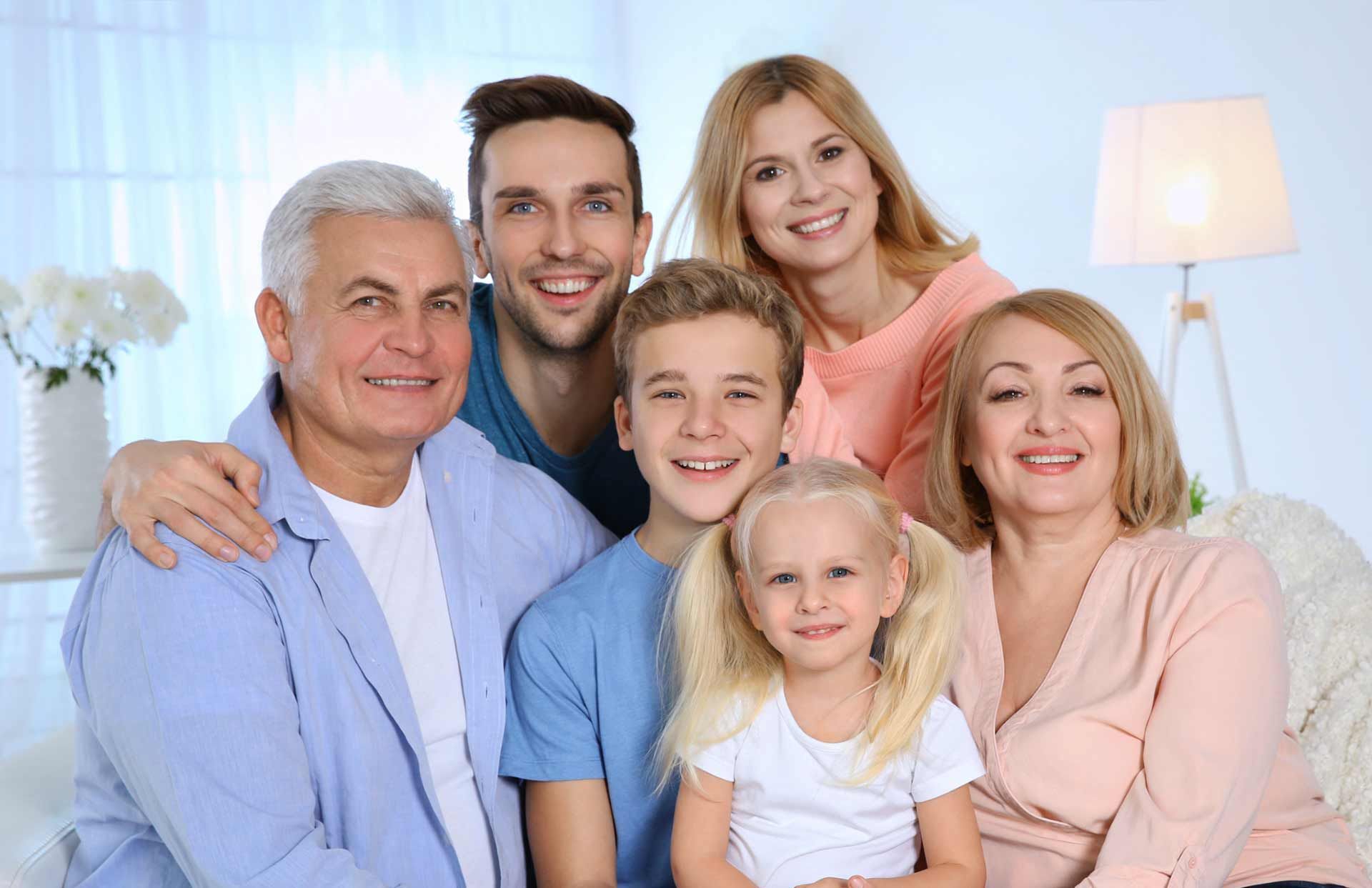 Smiling family group posing together on a couch in a bright living room.