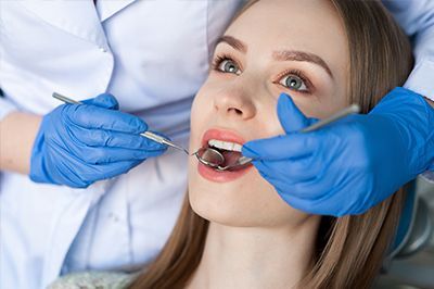 Dentist examining a patient’s mouth with blue gloves and dental tools in a clinic
