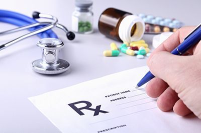 Handwriting a prescription on an Rx form with stethoscope, pills, and medicine bottles nearby