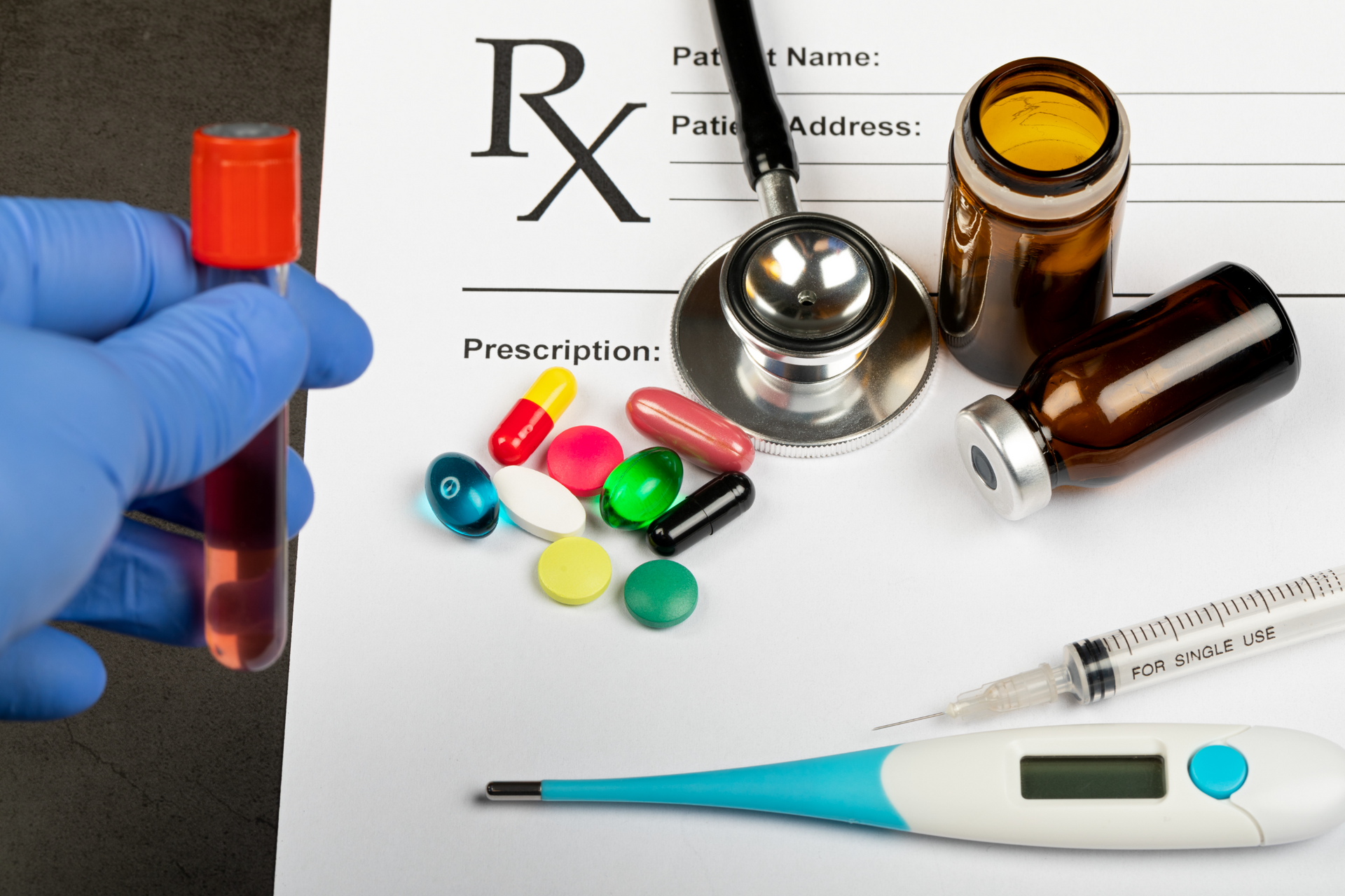 Medication and prescription items with pills, bottles, syringe, thermometer, and gloved hand on a table