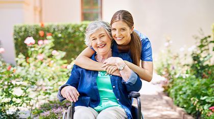 Smiling older woman in wheelchair with young woman hugging her outdoors in a garden
