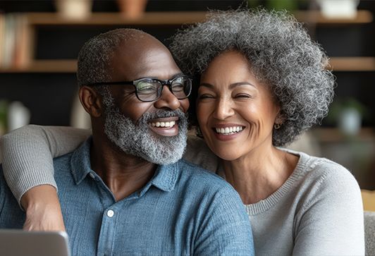 Smiling couple with gray hair sitting close together on a couch in a cozy living room.