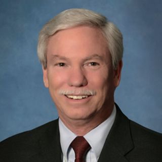 Portrait of a man in a dark suit and red tie against a blue studio background, smiling gently