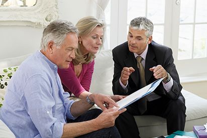 Three people in business attire reviewing documents together on a couch in a bright room