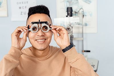 Person holding a pair of eyeglasses to their face in an optometry exam room