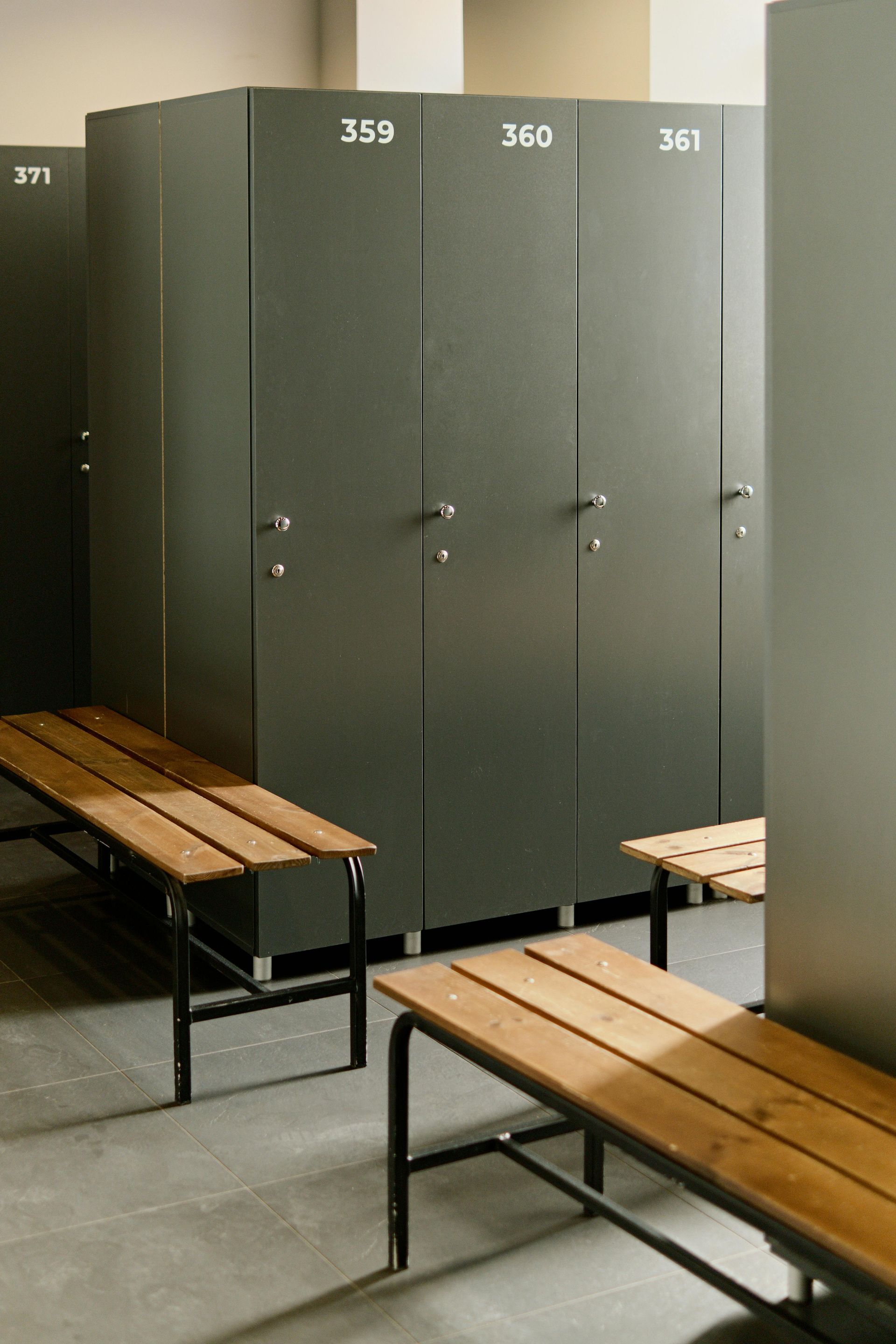 Gray lockers with numbers 359, 360, and 361 stand over wooden benches in a locker room.