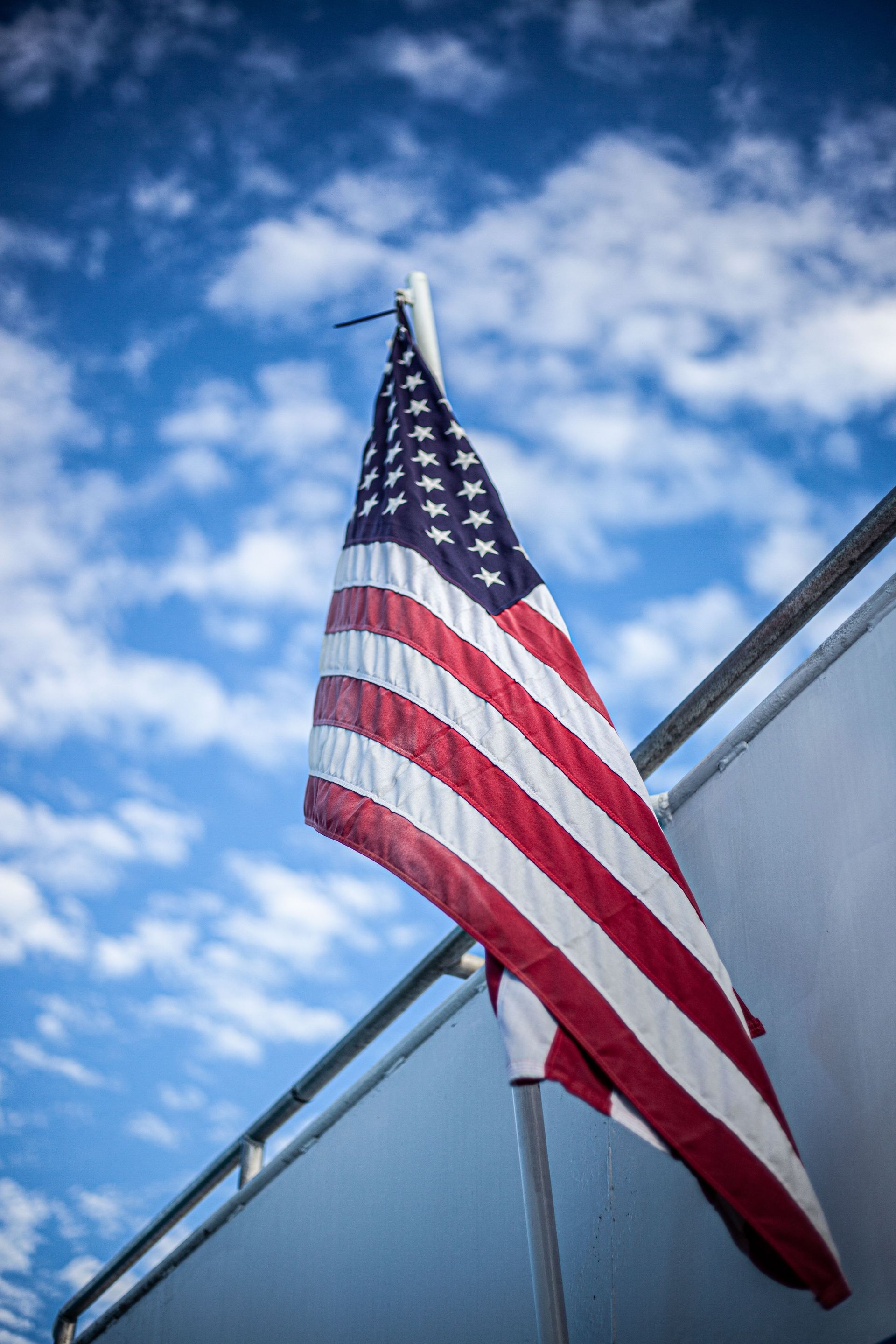 American flag on a pole against a blue sky, beside a building rooftop.