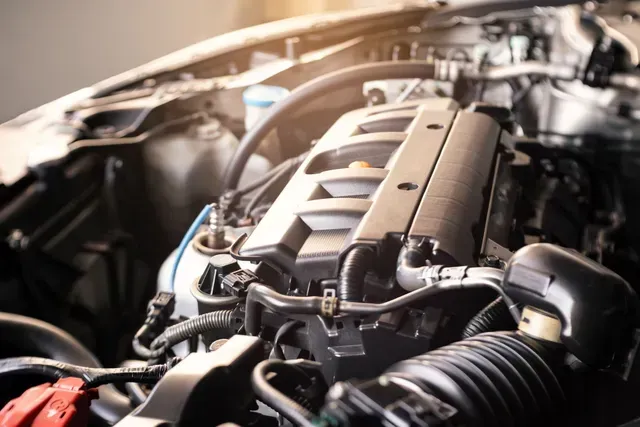 Close-up of a car engine bay with metallic engine components and hoses under warm light