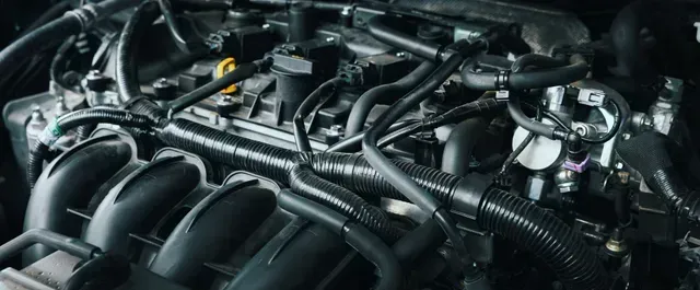 Close-up of a car engine bay with black hoses, wiring, and metal components | Motiv Auto Care