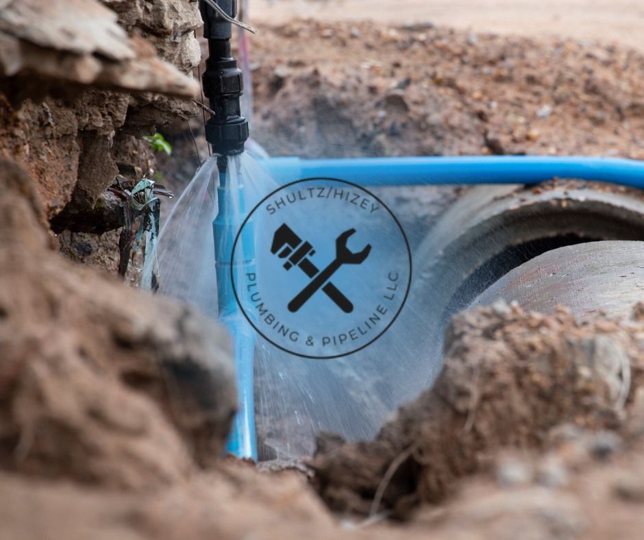 Blue water pipe leaking in a ditch. Schultz/Nizey Plumbing & Pipeline LLC logo visible.