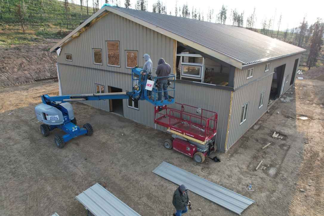 Workers installing metal siding on building using boom lift and scissor lift with gray panels