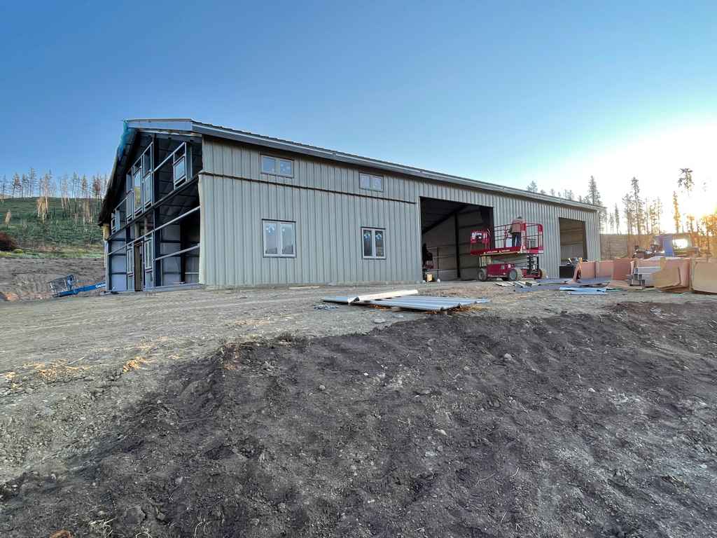 A large, light gray metal building under construction with open garage doors, windows, and a blue sky backdrop.