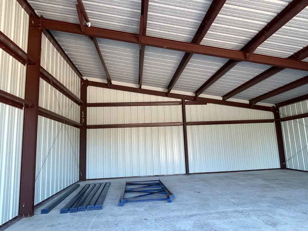 Interior of metal building frame with corrugated roof and walls on concrete floor with materials inside
