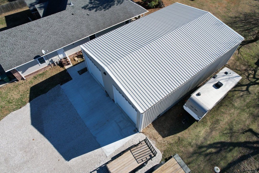 Aerial view of a two-car garage with a corrugated metal roof. A gravel driveway and trailer are next to the building.