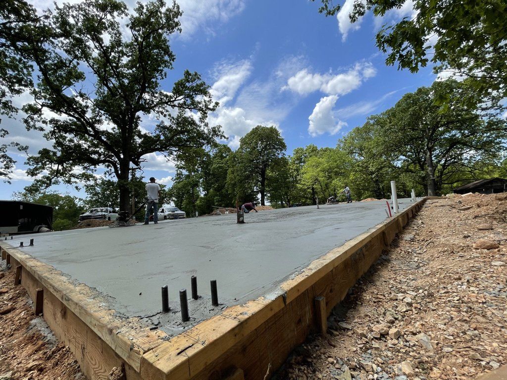 Fresh concrete foundation framed with boards with workers and trees under partly cloudy sky