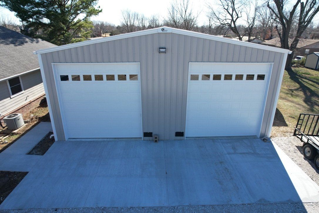 Two-car garage with white doors and light gray siding. Concrete driveway, suburban setting.