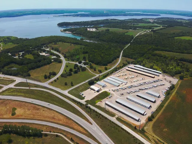 Aerial view of a storage facility lot with multiple rows of structures next to a road and a large lake in the background.