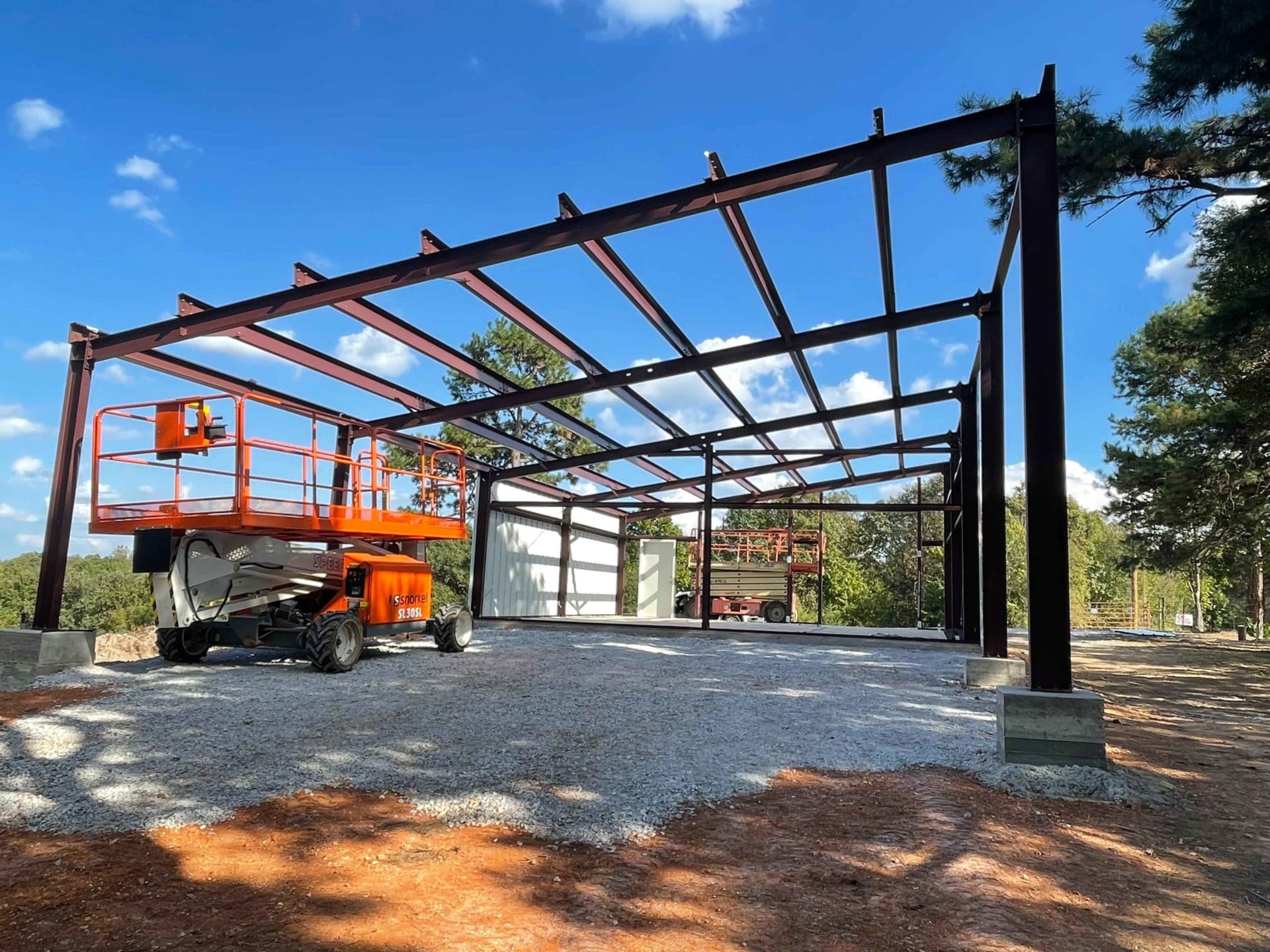 e metal building under construction with cherry picker on gravel foundation under blue sky