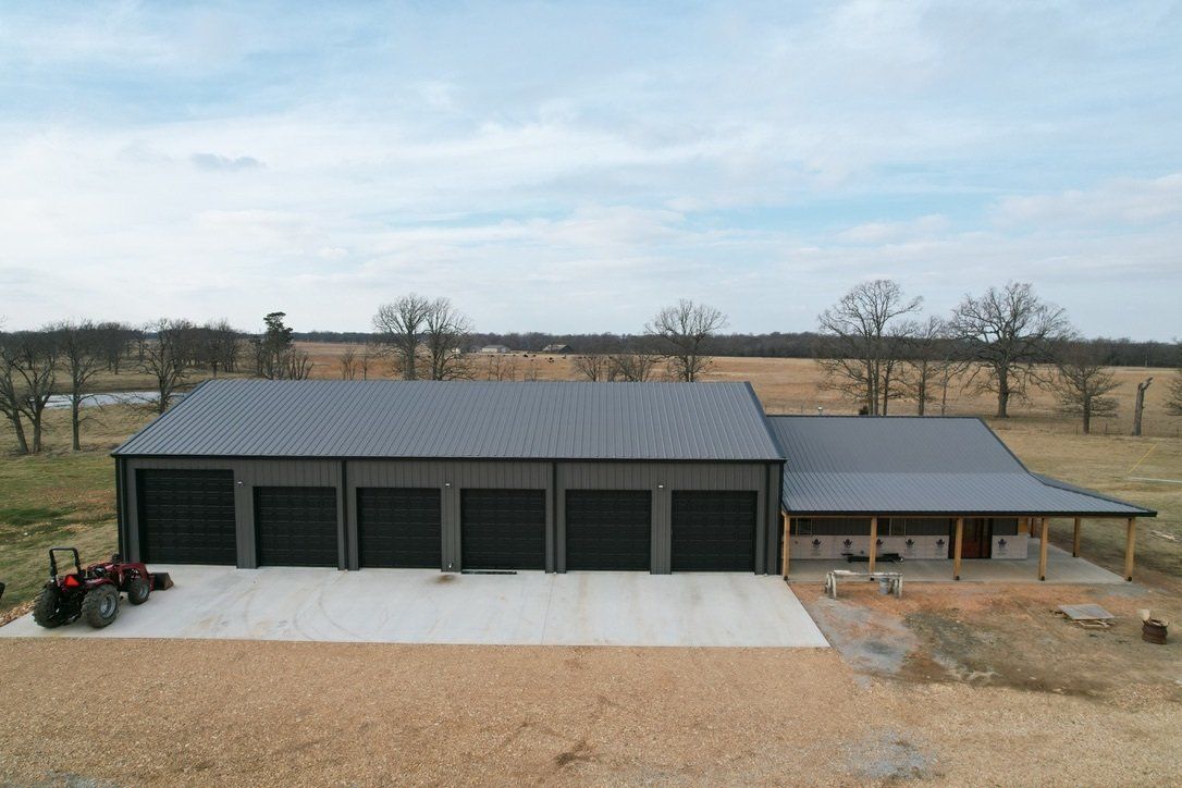 Large gray metal building with five garage doors and porch on concrete pad with tractor nearby