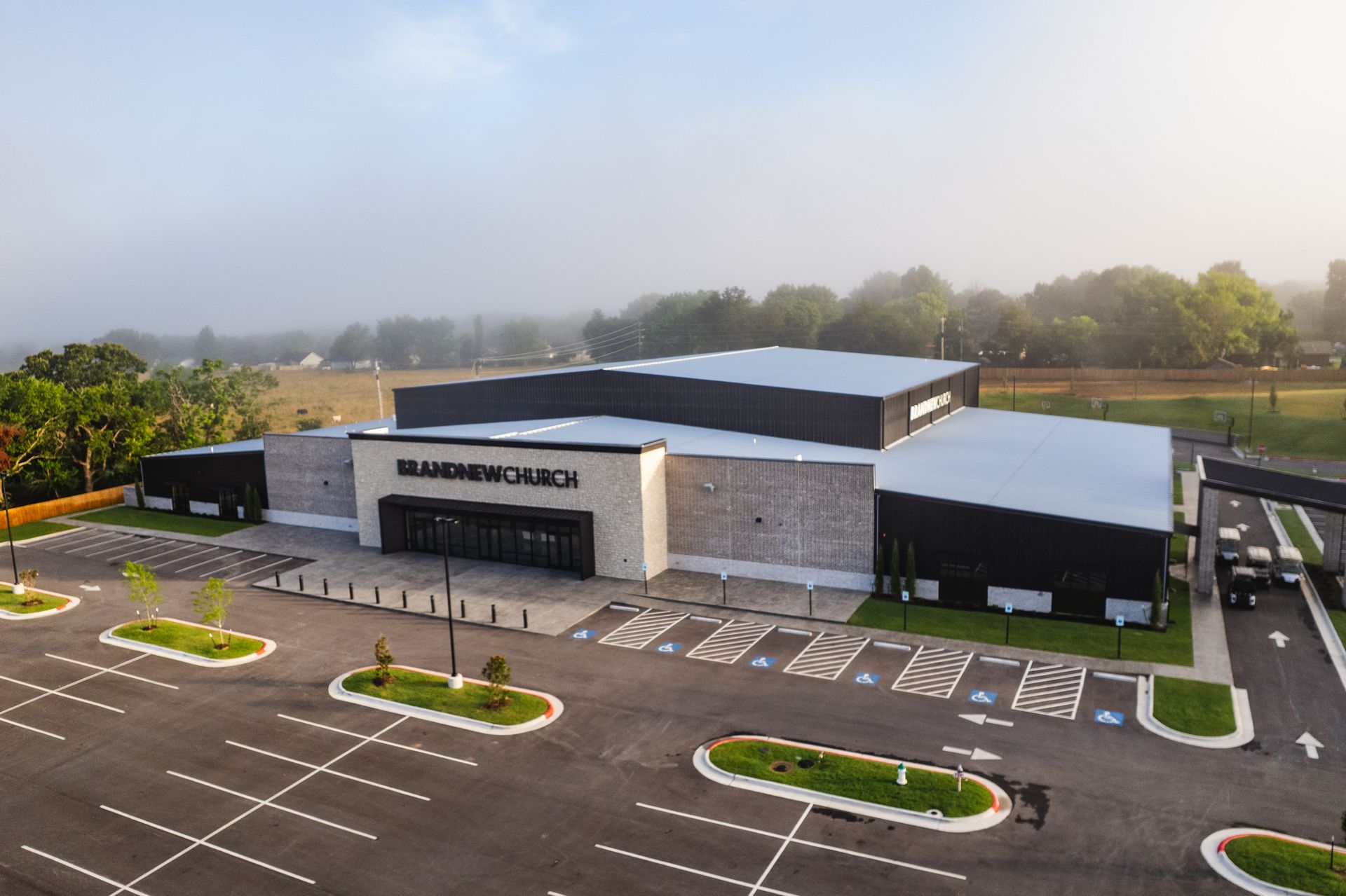 Aerial view of modern church building with brick facade and parking lot on foggy morning