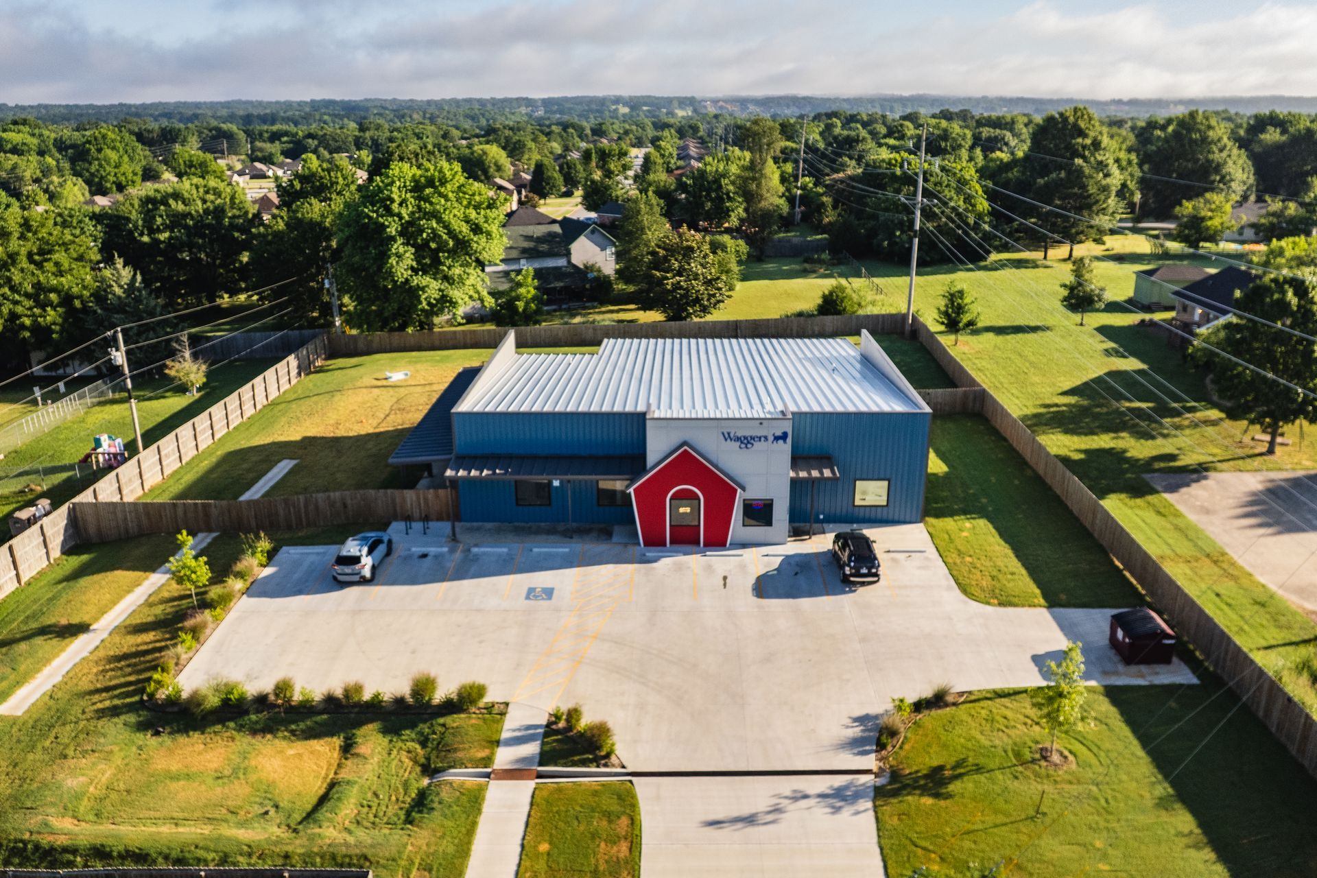 Aerial view of modern metal building with red entrance, blue and gray exterior, and large parking lot