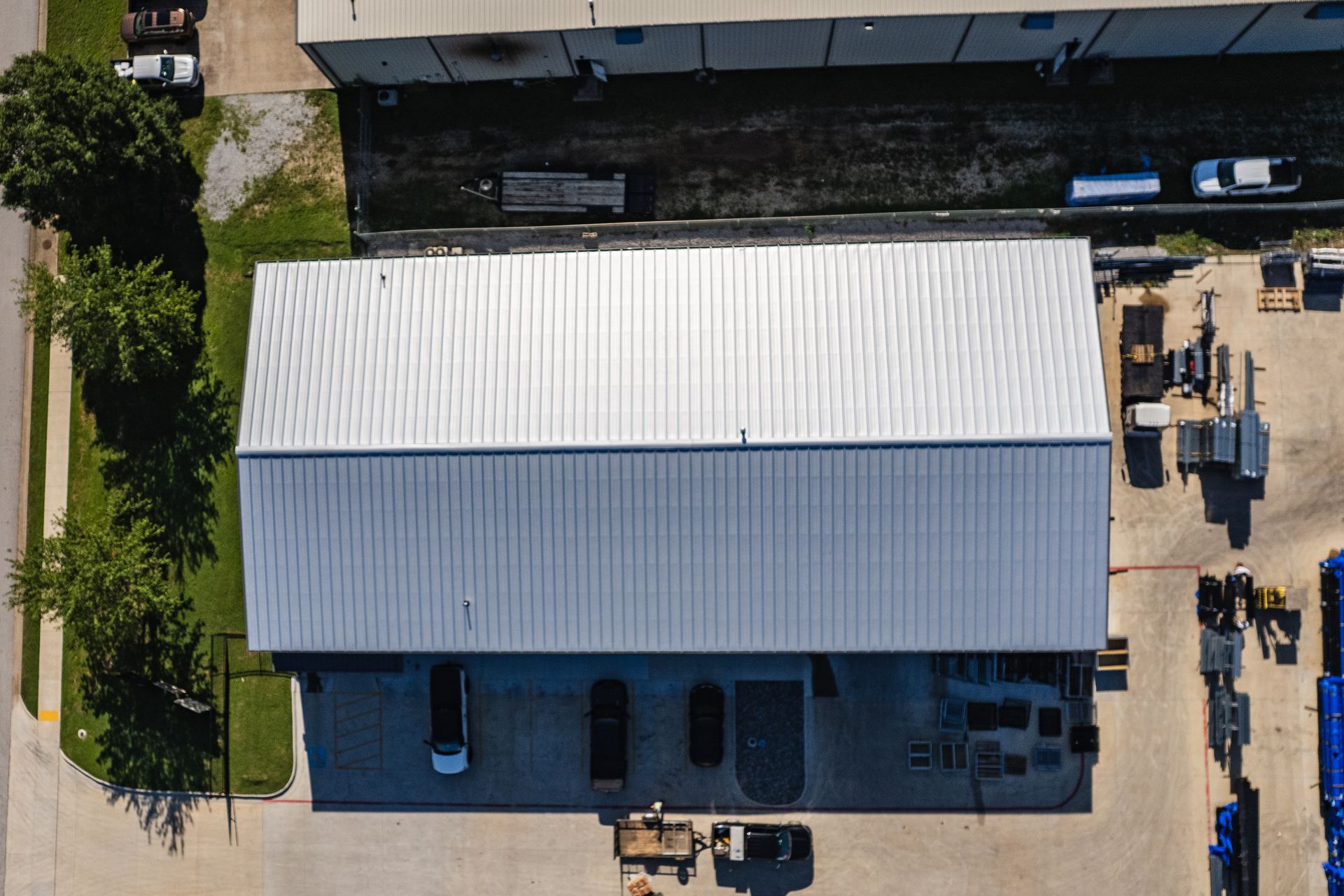 Aerial view of large industrial metal building with silver roof, equipment, and asphalt and grass areas