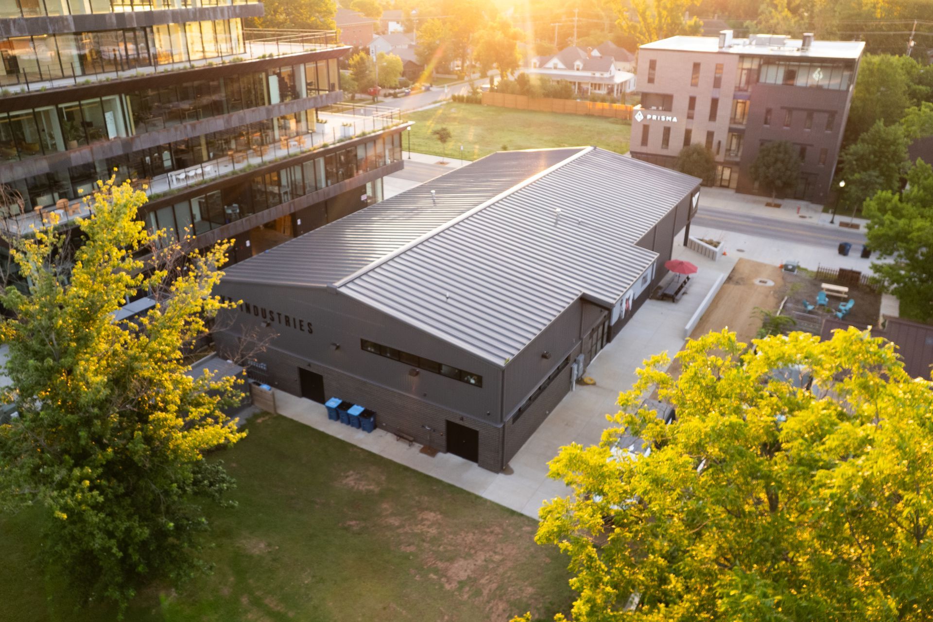 AnAerial view of modern black metal building with curved roof in tree-lined area at sunset