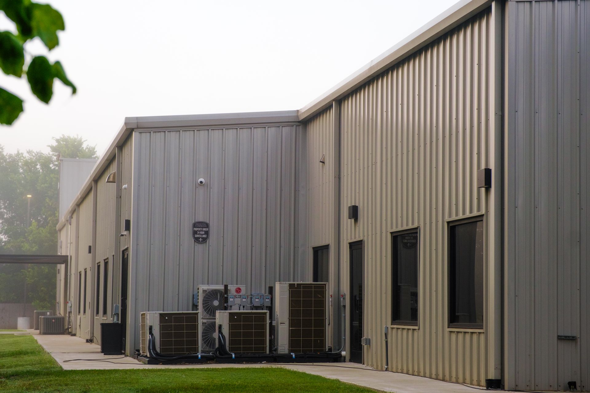 Light metal building with flat roof, windows, and AC units along side on grassy area