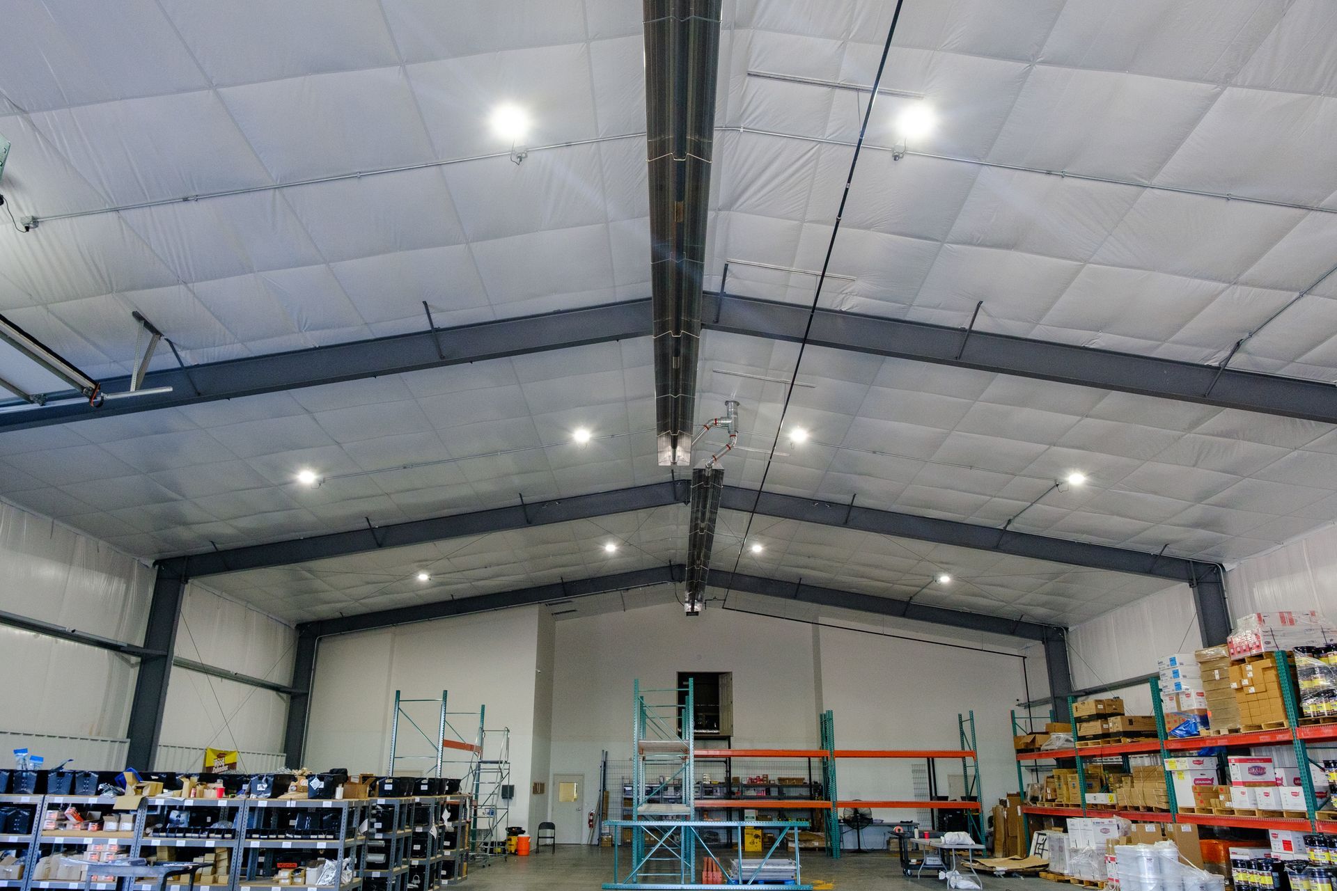 Warehouse interior with high ceilings, metal beams, bright lighting, and stocked shelving