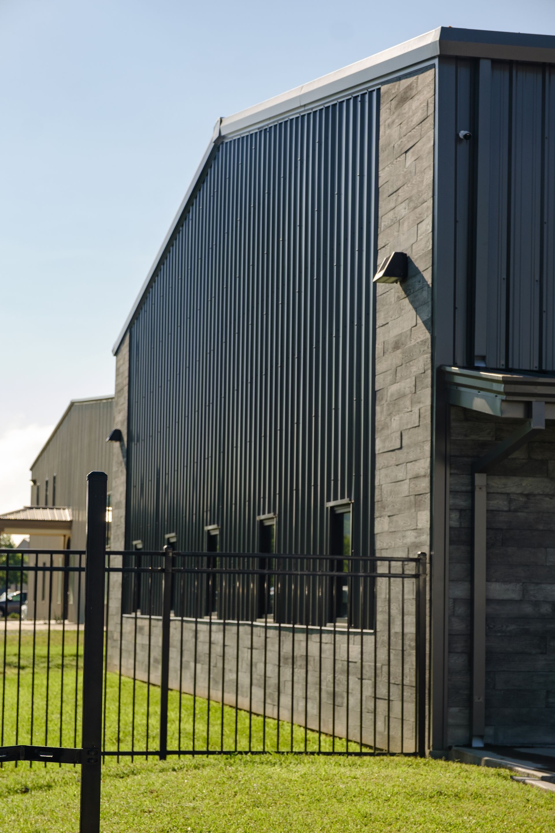 Modern metal building with wavy corrugated siding, gray brick facade, and fence on grassy lawn