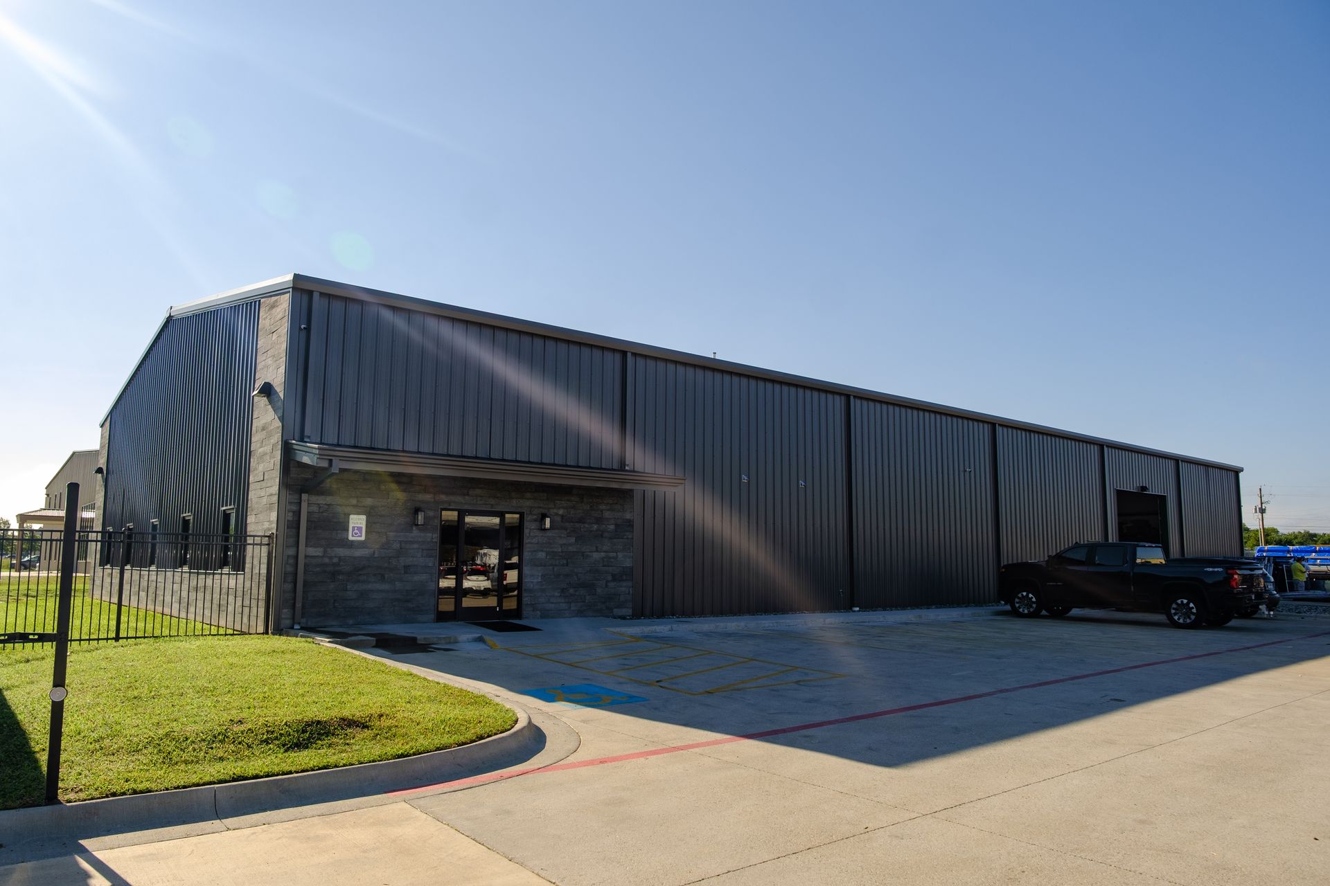 Long dark commercial metal building with entrance and black pickup truck under blue sky