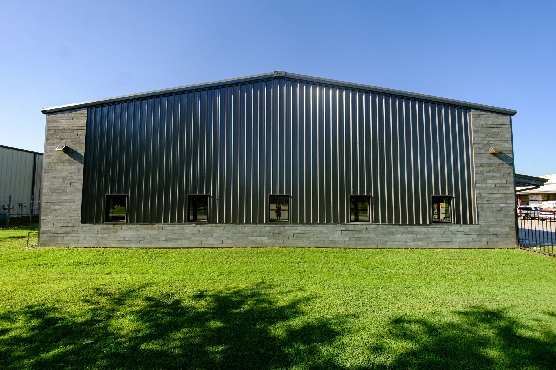 Metal building with black corrugated roof and walls, gray brick sides, and small windows on green lawn