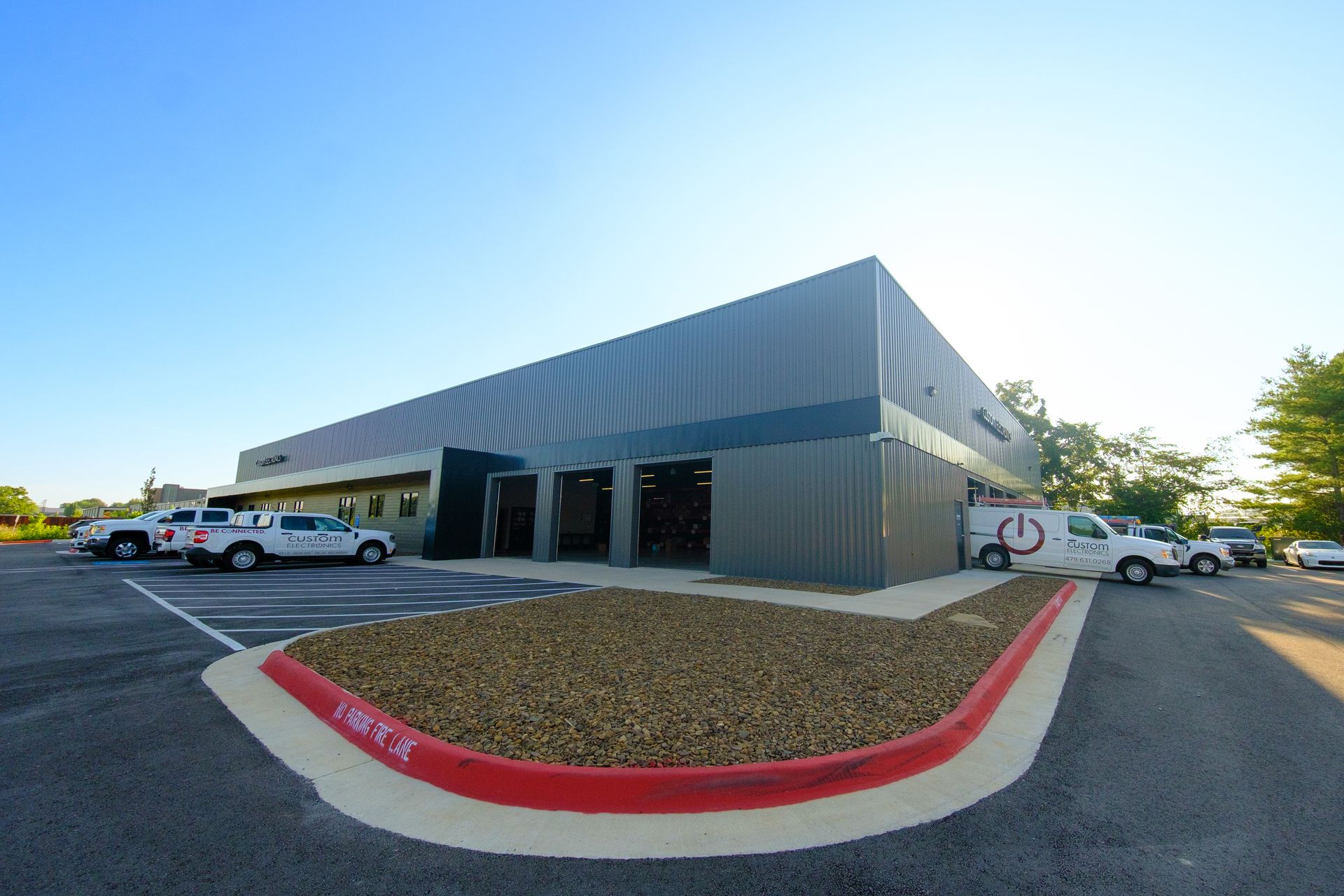 Modern metal building with gray siding, open garage bays, and trucks parked under blue sky