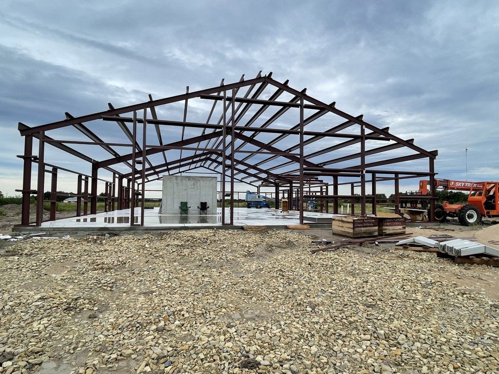 Steel frame metal building under construction on gravel lot with concrete foundation and utility box