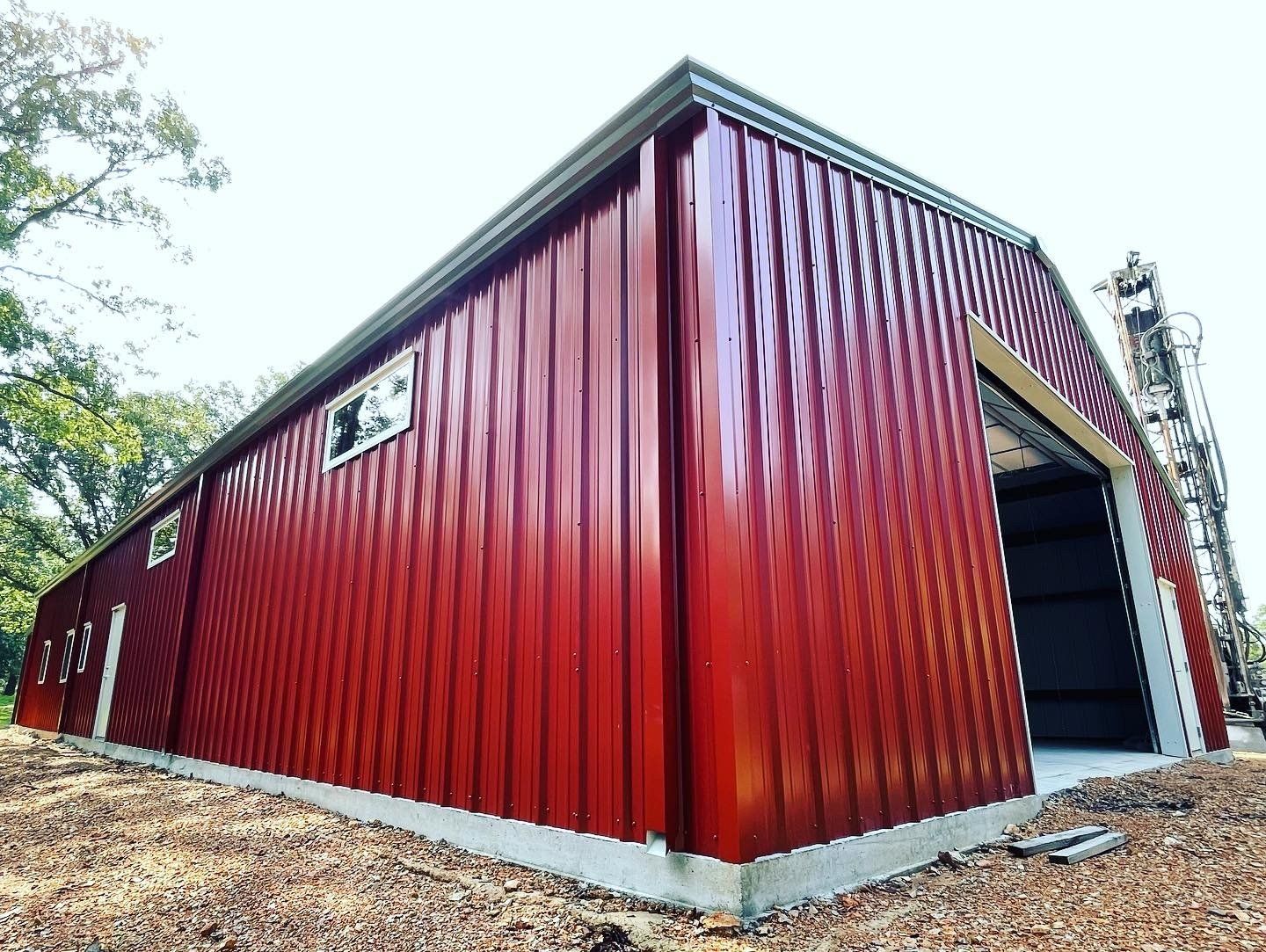 Red agricultural metal building with open door and windows on concrete foundation under clear sky