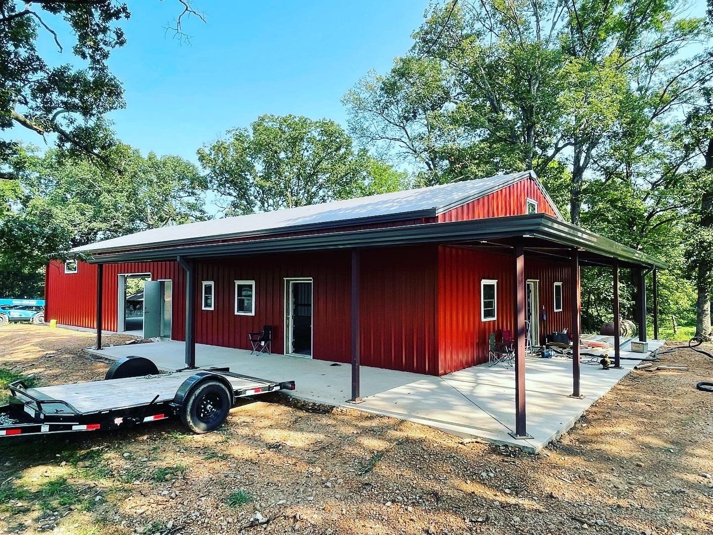Red metal building with a porch and a trailer parked outside on a sunny day.