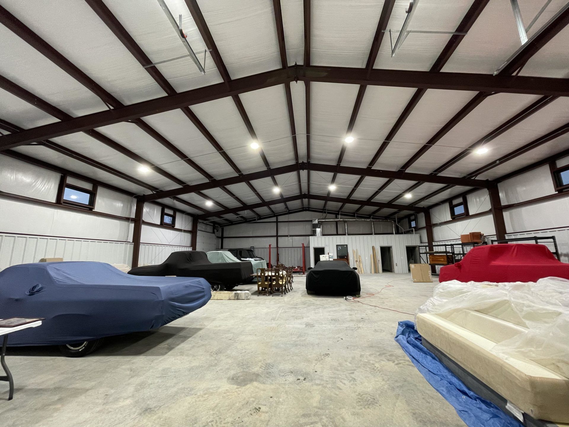 Interior of large metal building with covered cars, work tables, equipment, and overhead lighting