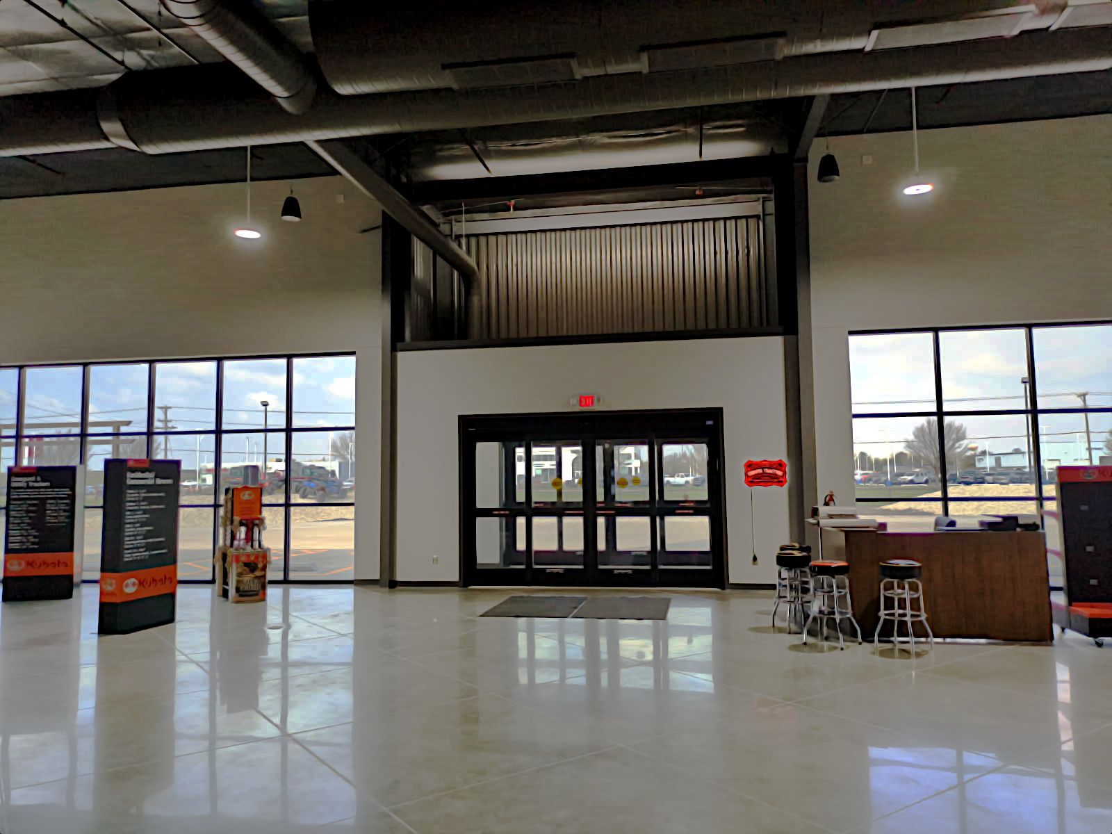 Modern lobby with glass doors, tall windows, stage area, reflective floors, and information displays