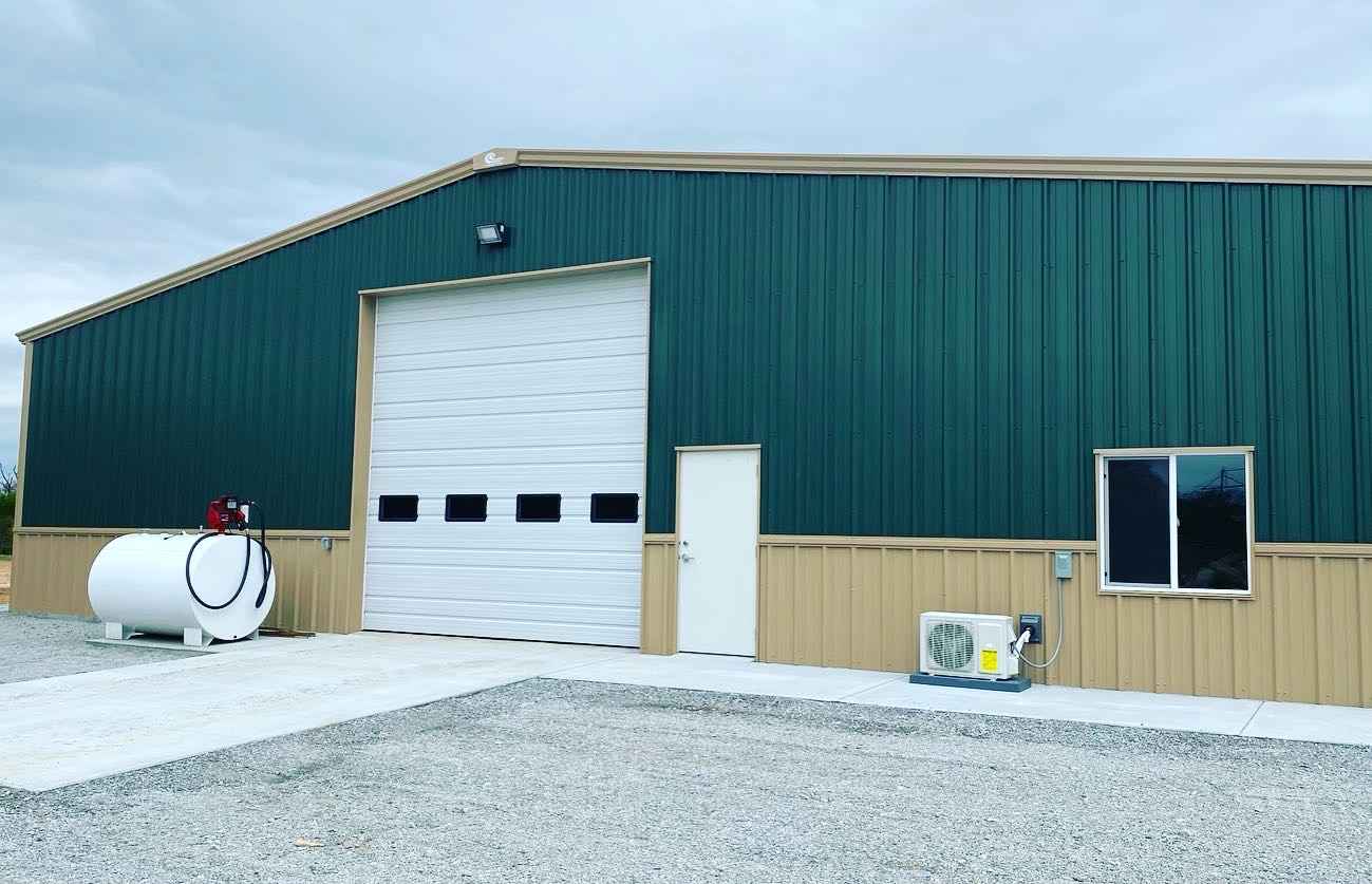 n metal building with white garage door, entry door, and window on gravel drive with tank and AC unit