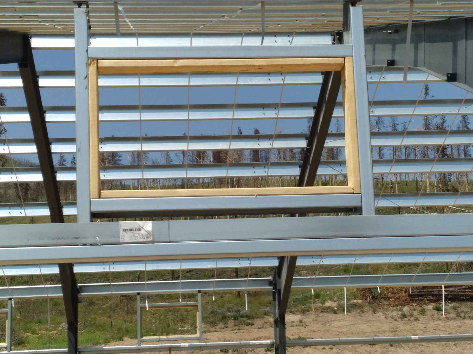 Wood framing inside metal building structure for window opening with steel grid and outdoor view