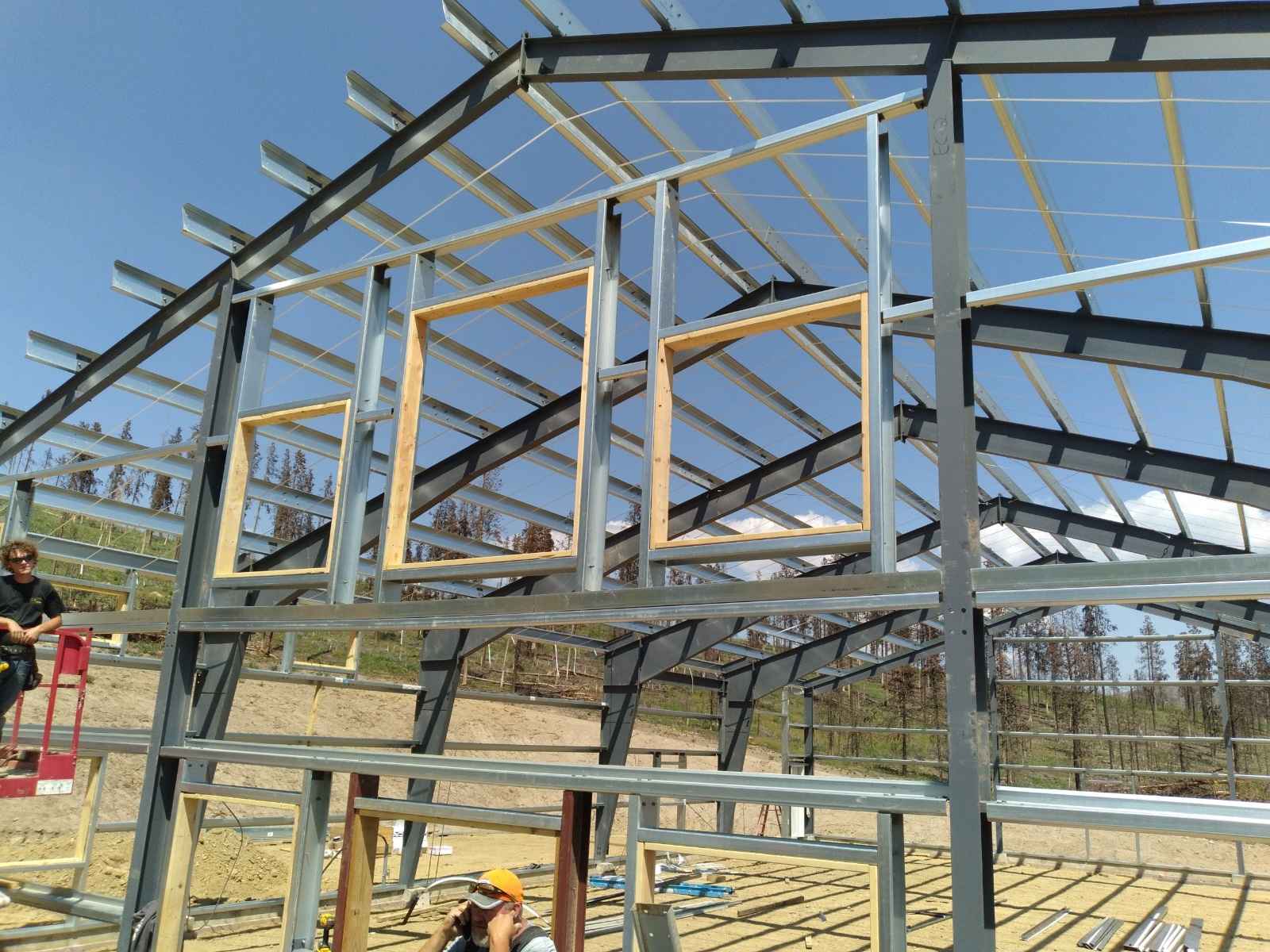 Metal building frame under construction with wood window frames, lift, and worker in hardhat