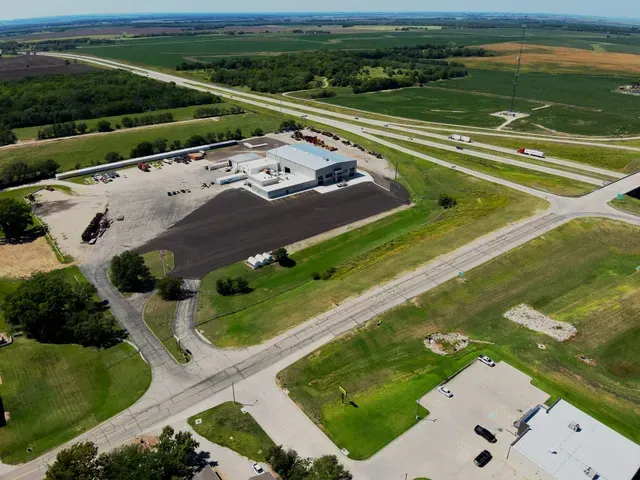 Aerial view of a commercial building with a paved lot, near a highway and rural fields.