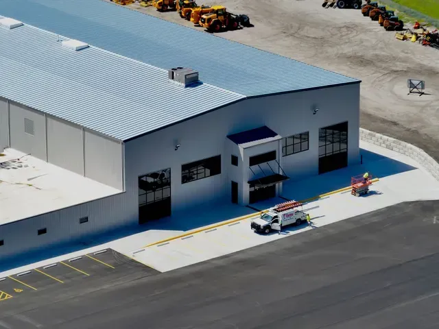 Aerial view of white industrial metal building with parking lot, equipment, and work truck in front