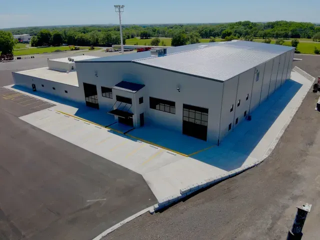 An aerial view of a white, rectangular industrial metal building with a metal roof and paved parking lot.